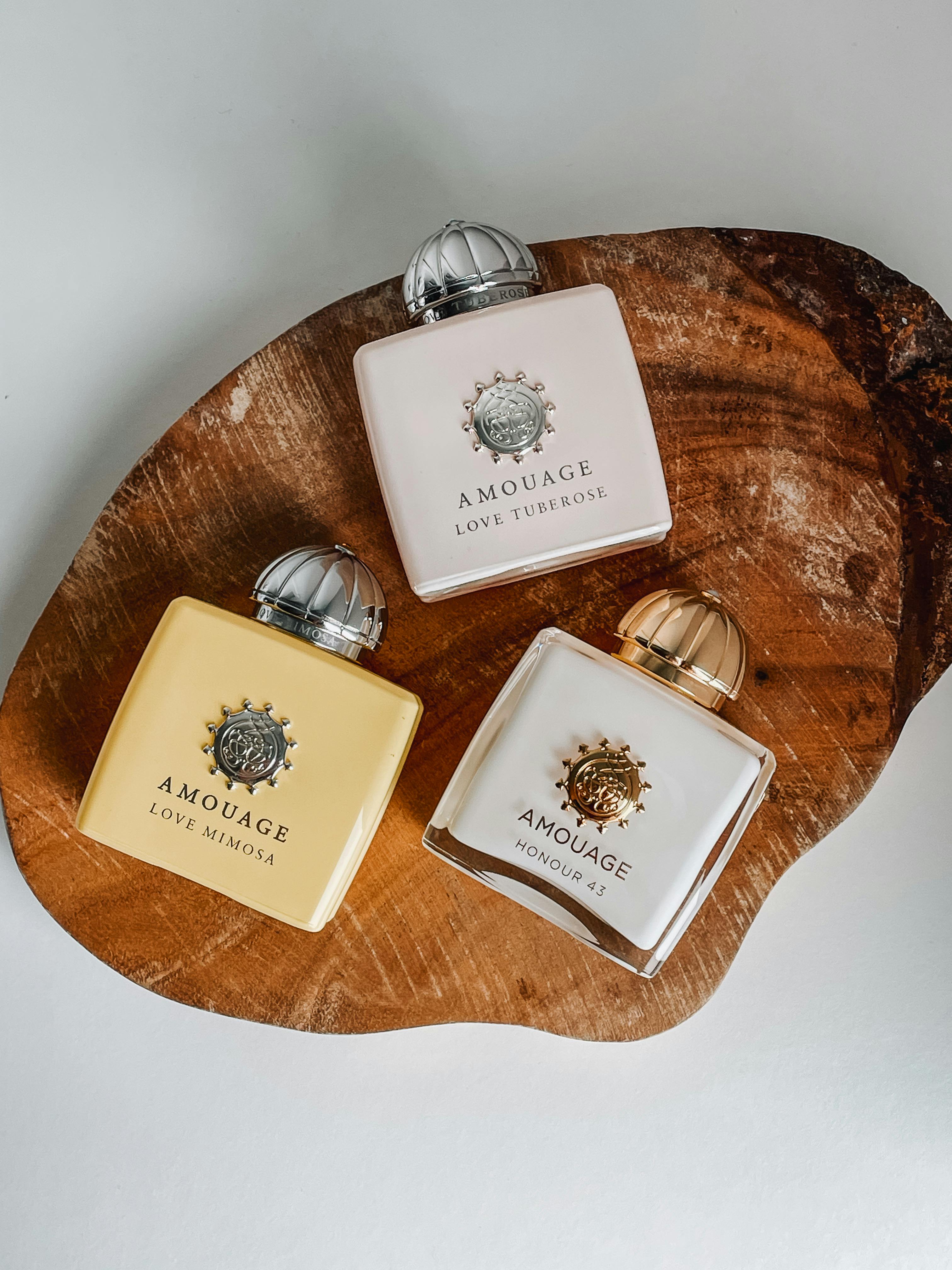 Three Amouage perfume bottles elegantly displayed on a wooden board.