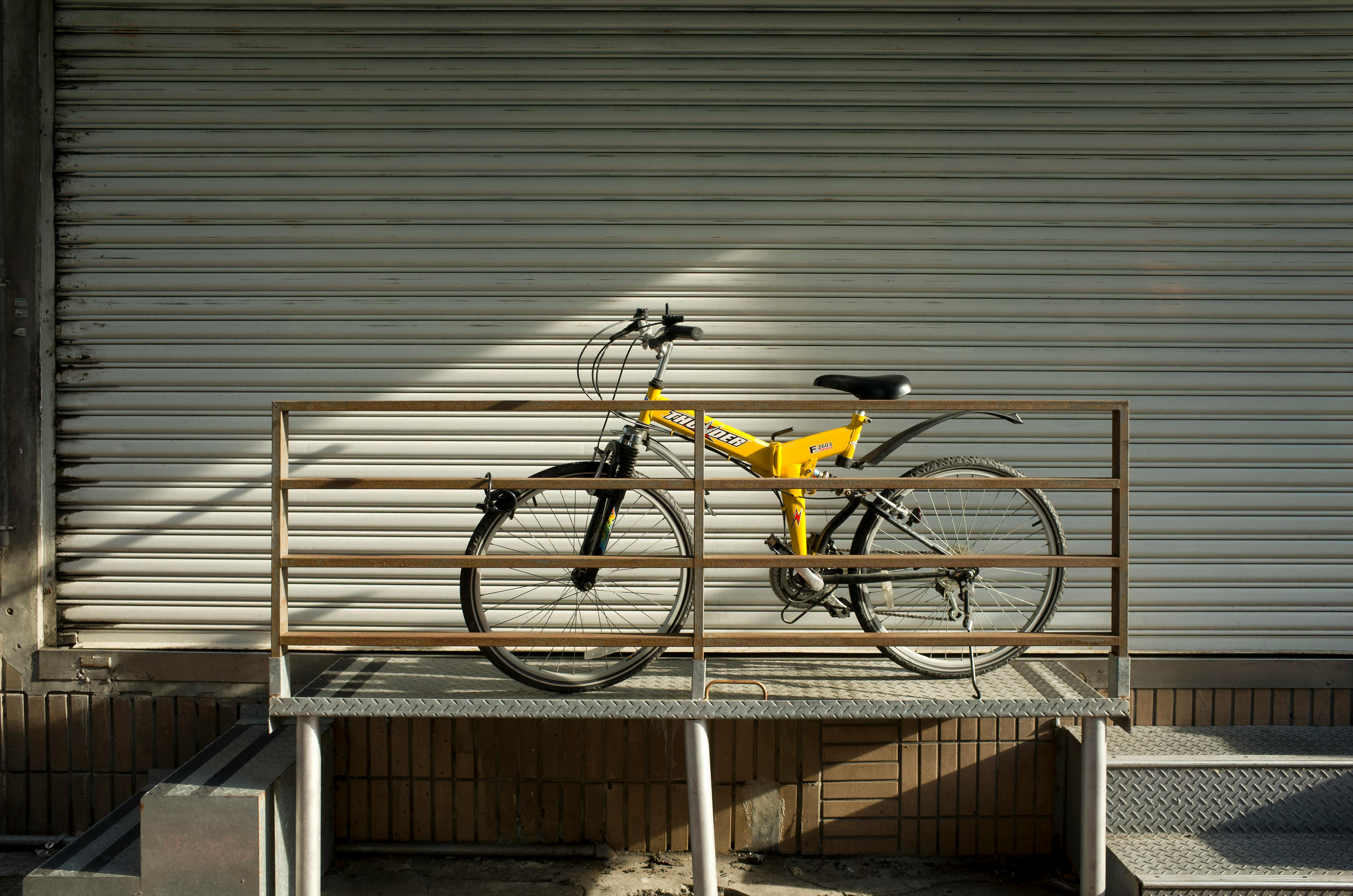 A yellow bicycle parked against metal shutters in the urban streets of Taipei, Taiwan.