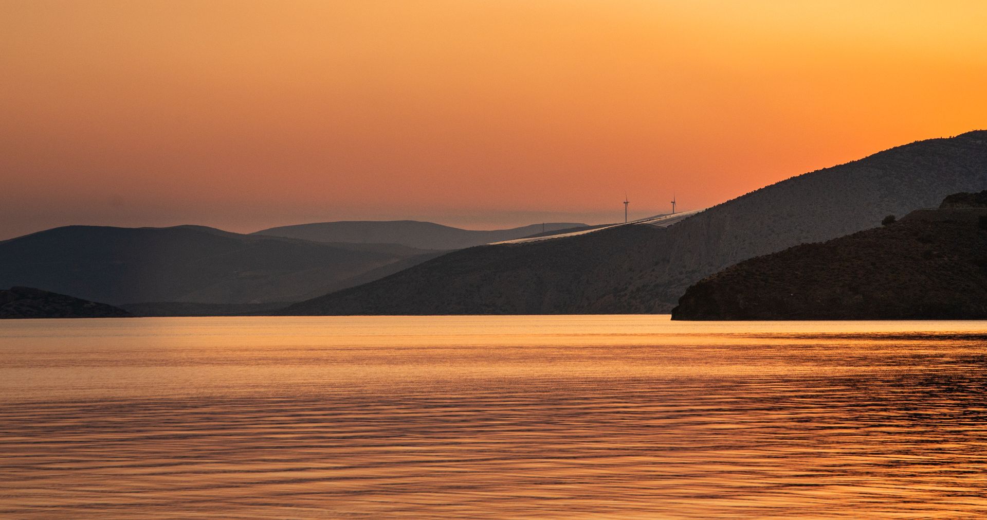 Stunning sunset over the Corinthian Gulf with wind turbines silhouetted against an orange sky.