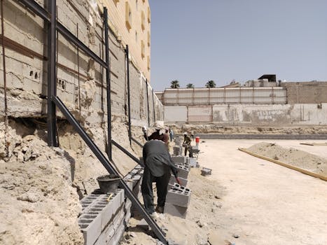 Workers building a concrete block retaining wall at a construction site under the clear sky.