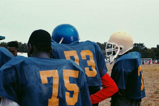 Teenagers in football gear during practice on a sports field.