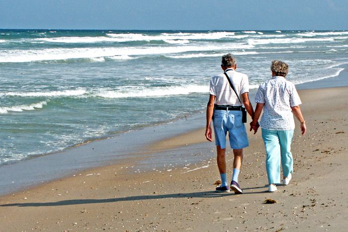 Dos personas mayores caminando tranquilamente junto al mar