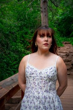 A woman in a floral summer dress poses on a wooded path in Boulder, Colorado.