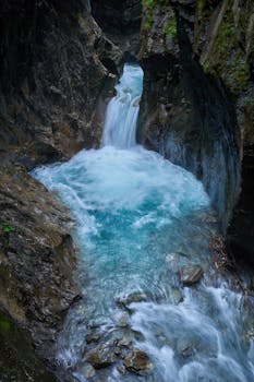 Captivating waterfall inside Kaprun Gorge, Austria, showcasing vibrant turquoise waters and rugged rocky cliffs.