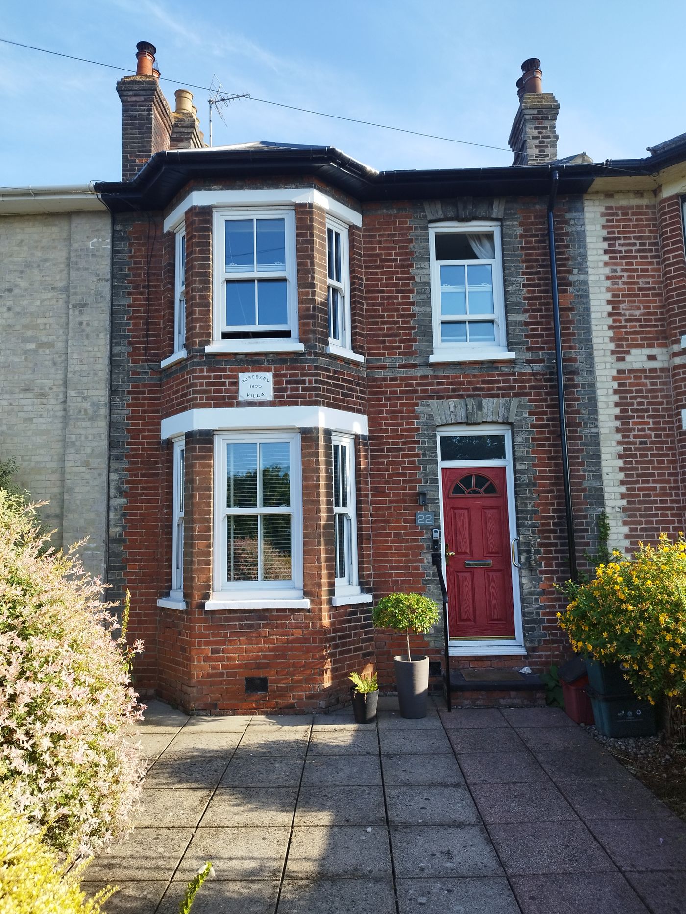 A red-brick house with a red front door and bay windows