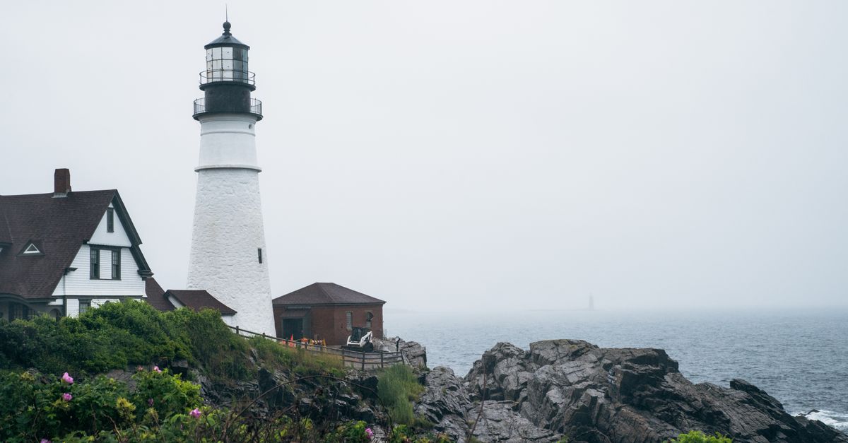 Iconic Portland Head Light with ocean view and rocky coastline in Maine on a misty day.