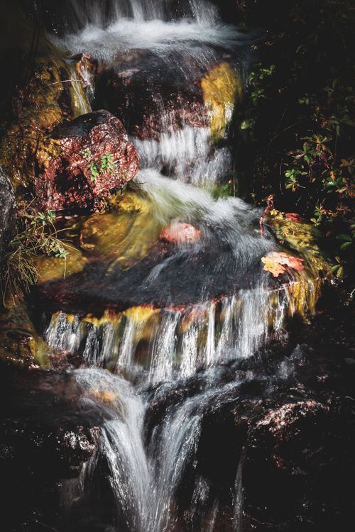 Free Captivating waterfall cascading over rocky terrain surrounded by lush greenery. Stock Photo
