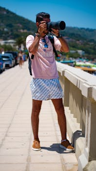 Man with camera on Sicily boardwalk capturing beach scenery on a sunny day.