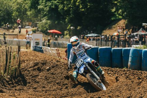 Free Motocross rider takes a sharp turn on a dirt track during a sunny motorsport event. Stock Photo