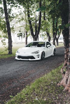 A modern white sports car parked on a tranquil forest path, framed by lush green trees.