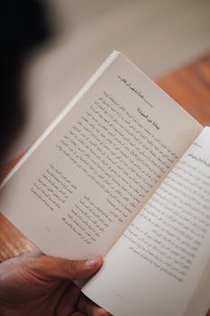 Person holding an open book with Arabic text, indoors.