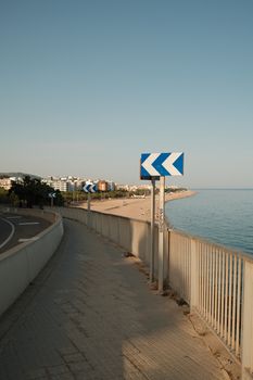 A tranquil coastal road with traffic arrows and ocean view at sunrise, offering a serene travel vibe.