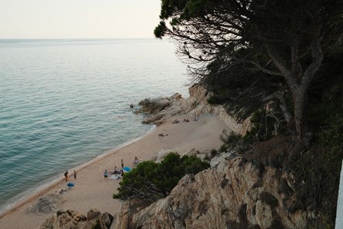 Free A serene Mediterranean beach with swimmers enjoying the clear water and rocky landscape. Stock Photo