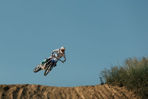Free A motocross rider performs an aerial stunt on a dirt track against a clear blue sky. Stock Photo