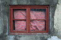 在台北的一堵混凝土墙上，有一扇饱经风霜的红框窗户，挂着红白条纹的窗帘
