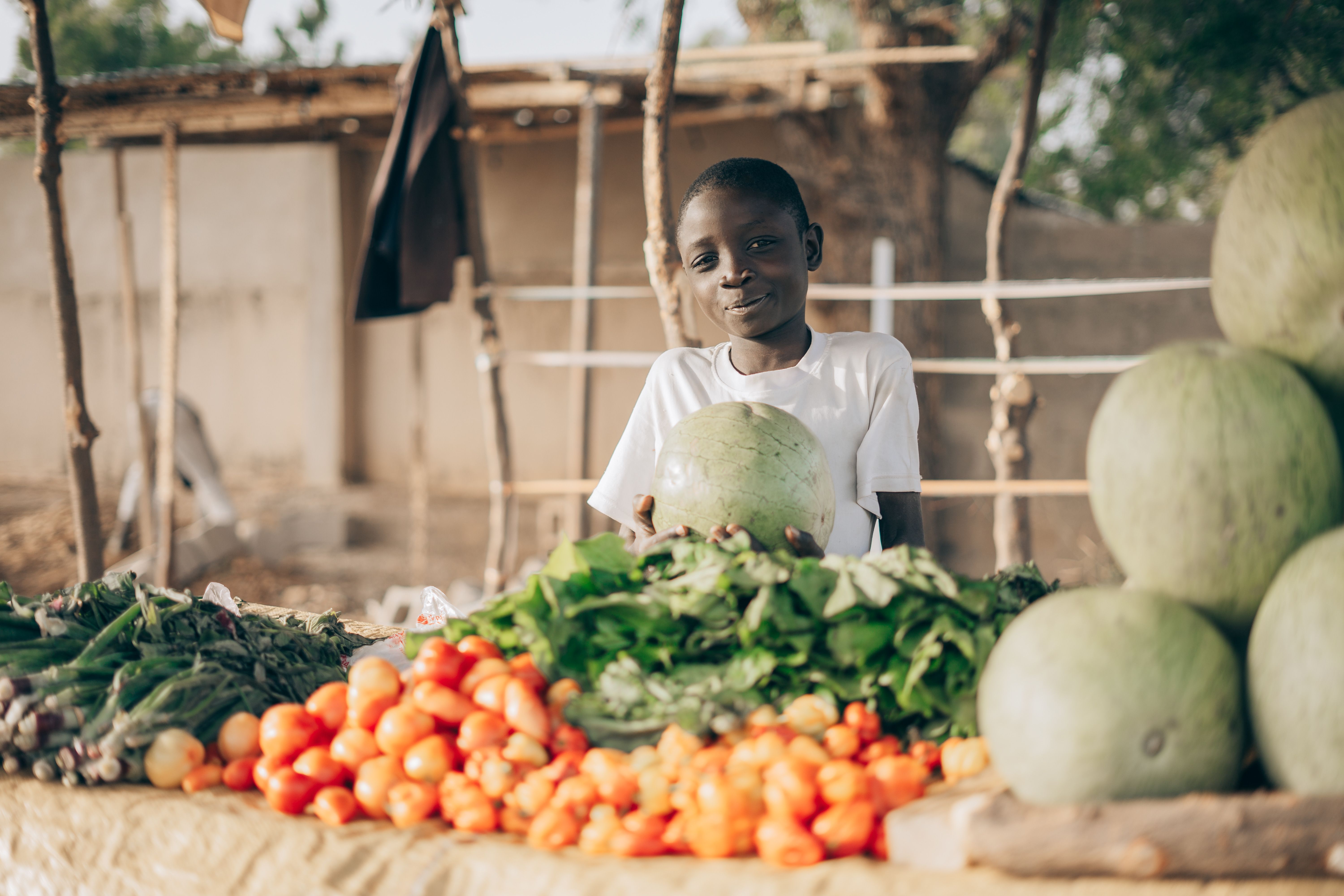 Un jeune vendeur présente ses légumes et pastèques sur son étal