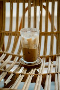 Glass of iced coffee with straw on rustic wicker chair, perfect for summer vibes.