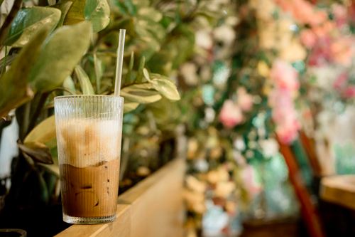 Free Refreshing iced coffee with a straw in a lush, floral garden setting. Stock Photo
