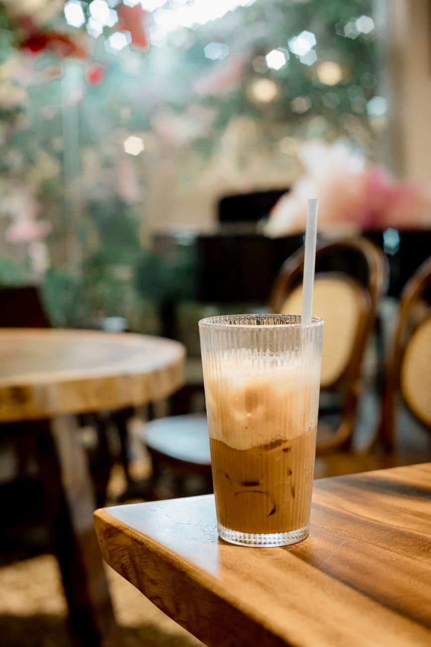 A refreshing iced coffee served in a glass tumbler with a straw on a wooden table in a cozy cafe ambiance.