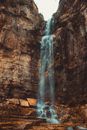 Spectacular view of high mounts with uneven bristly surface and fast cascade with transparent water flow under sky