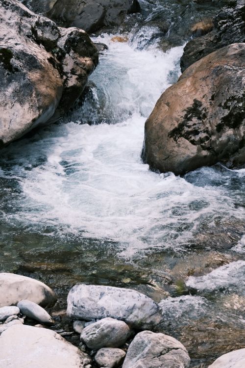 Free A serene mountain stream flows through moss-covered rocks, creating peaceful ripples in a natural setting. Stock Photo