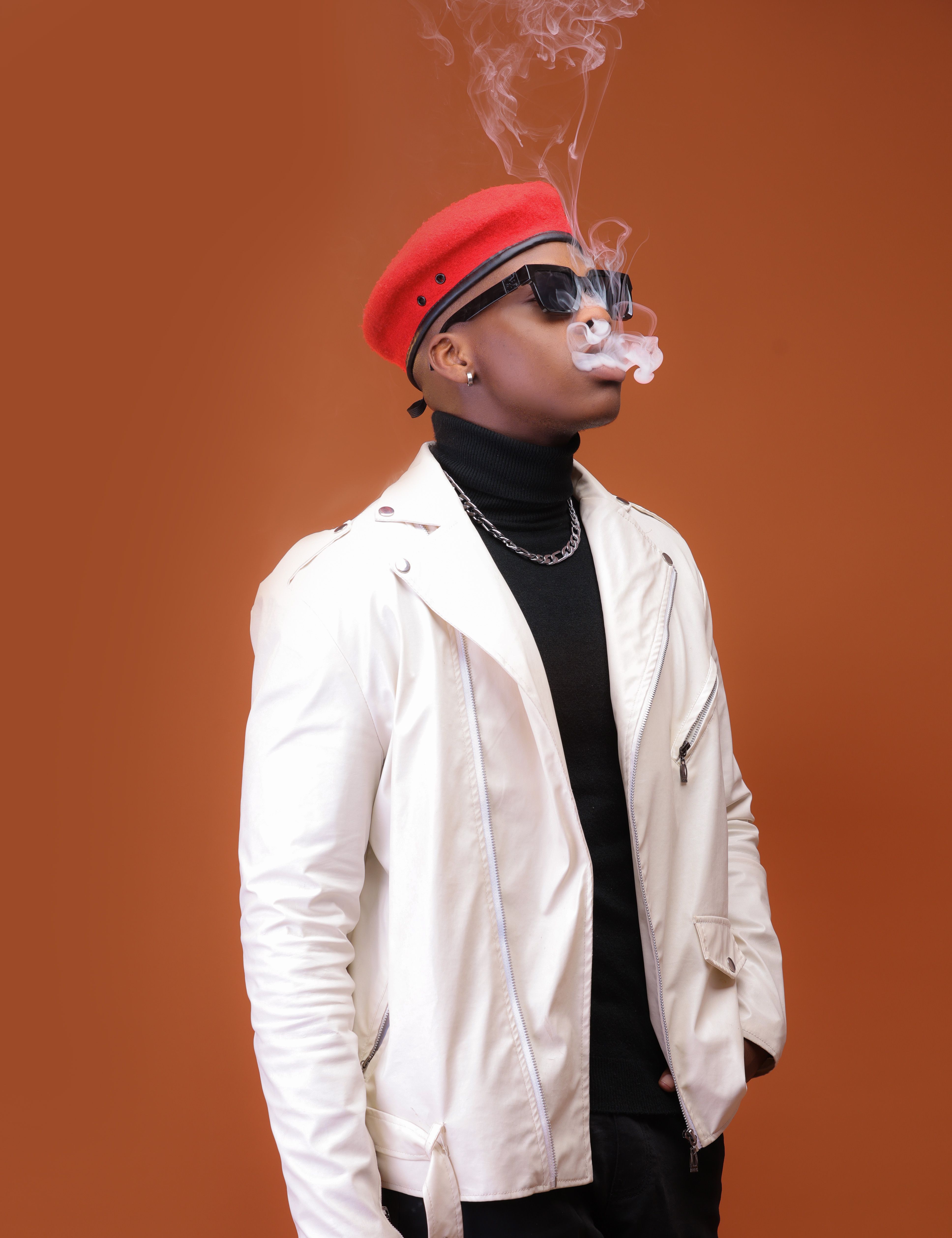 Fashionable man wearing sunglasses and a red beret, exhaling smoke.