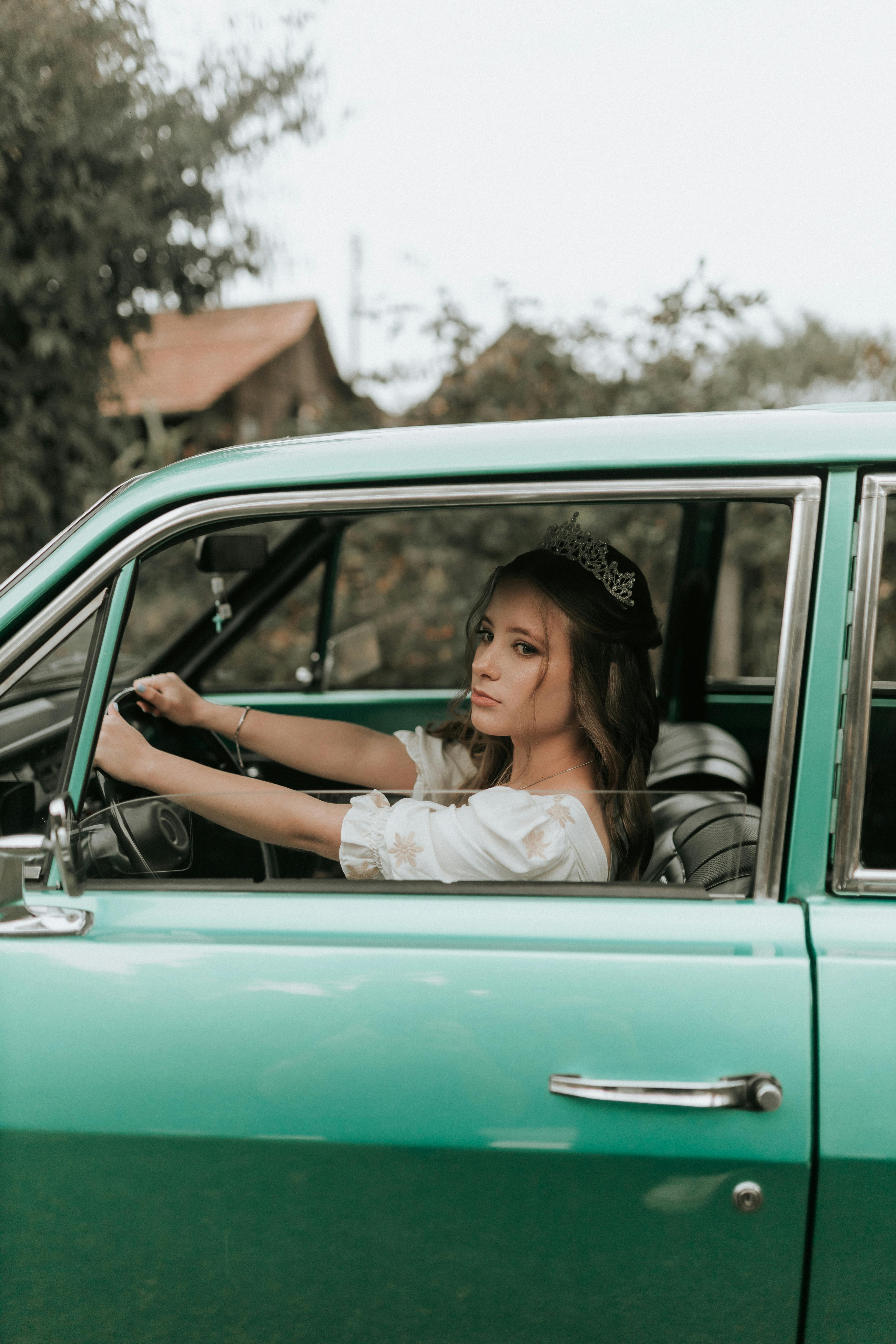Young woman in retro car showcasing vintage style with green vehicle outdoors.