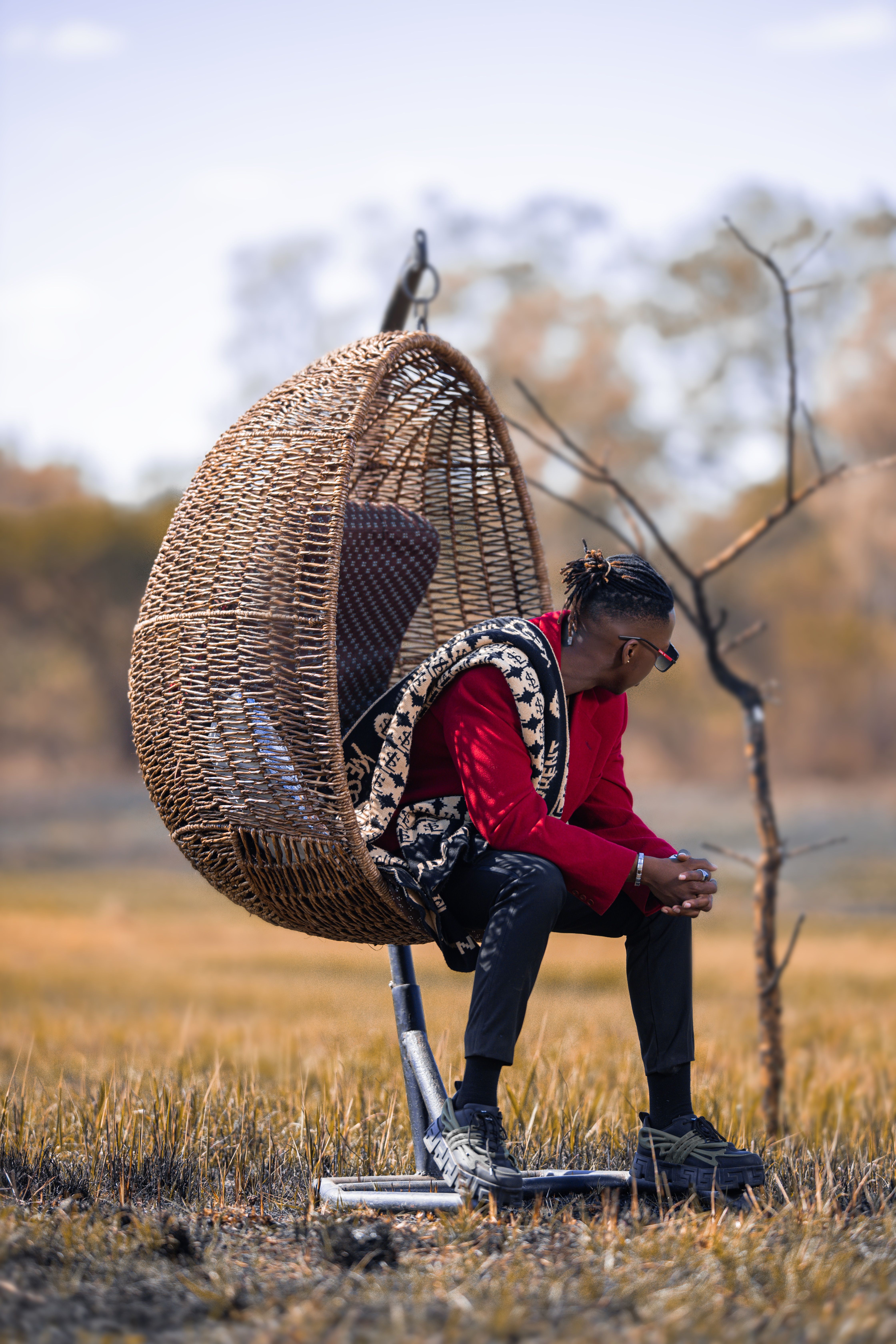 Individual sitting in a wicker swing chair in a serene outdoor setting.