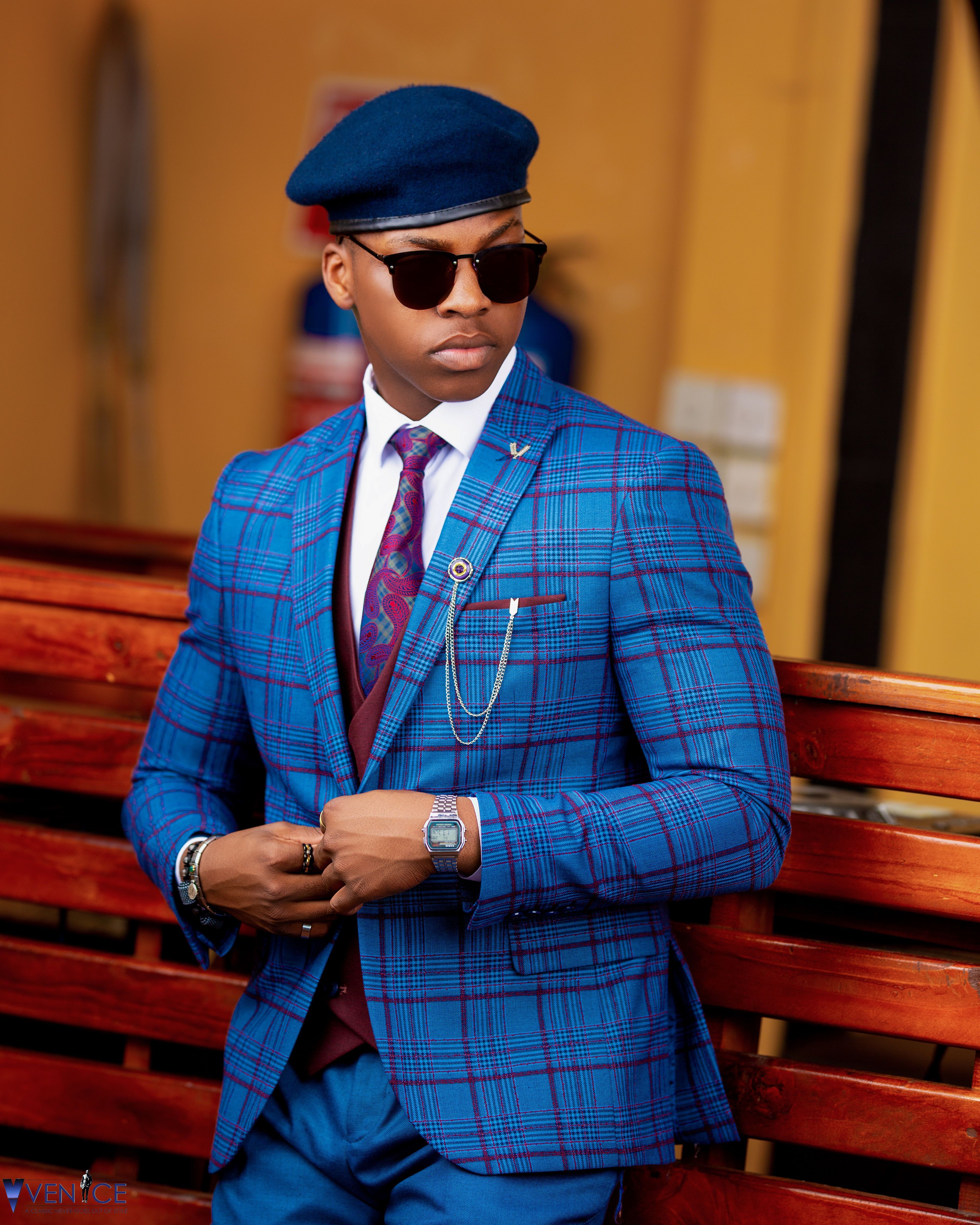 Elegant black man in a blue plaid suit with hat and sunglasses outdoors.