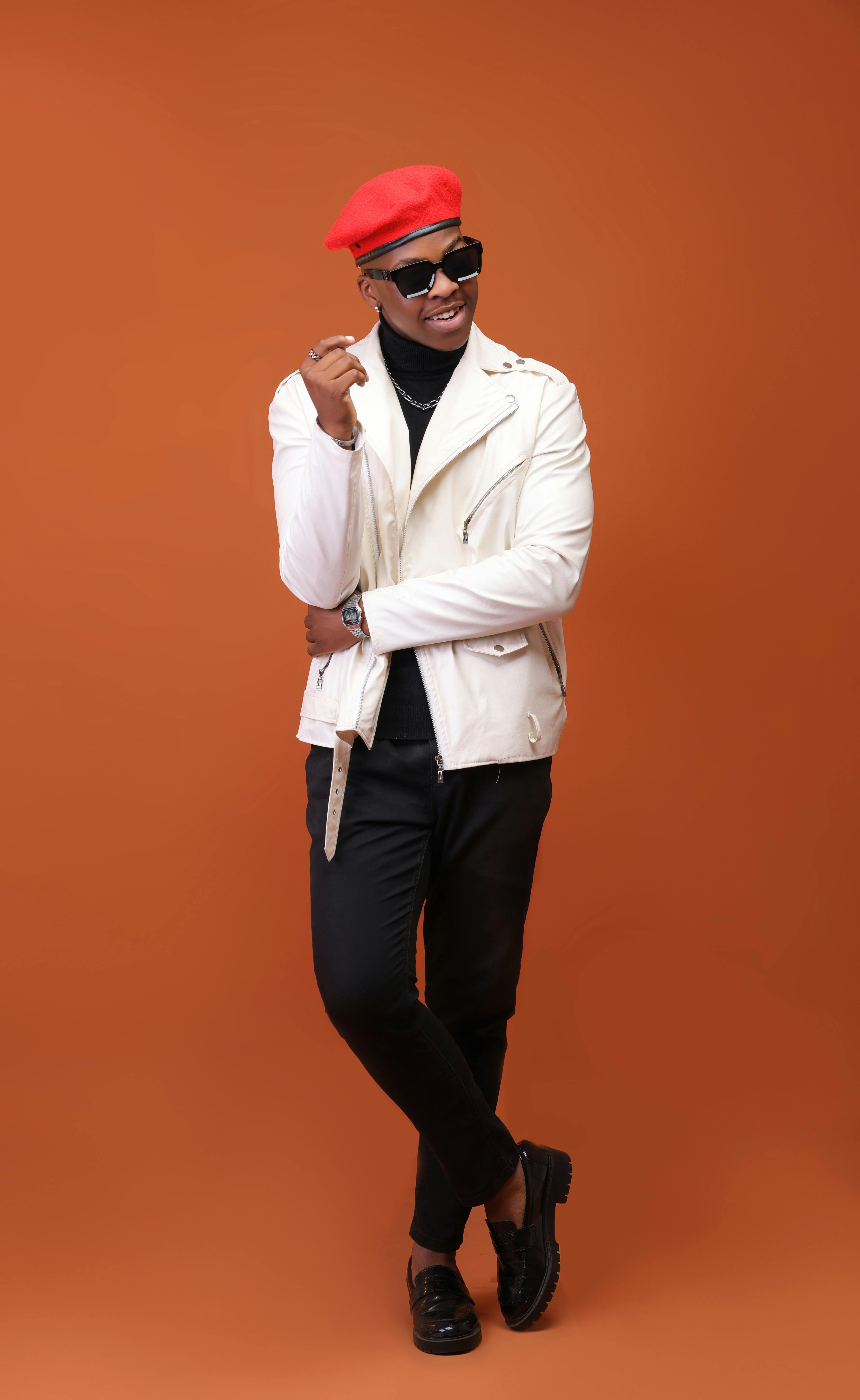 Fashionable portrait of a black man wearing a red beret and white jacket against an orange background.