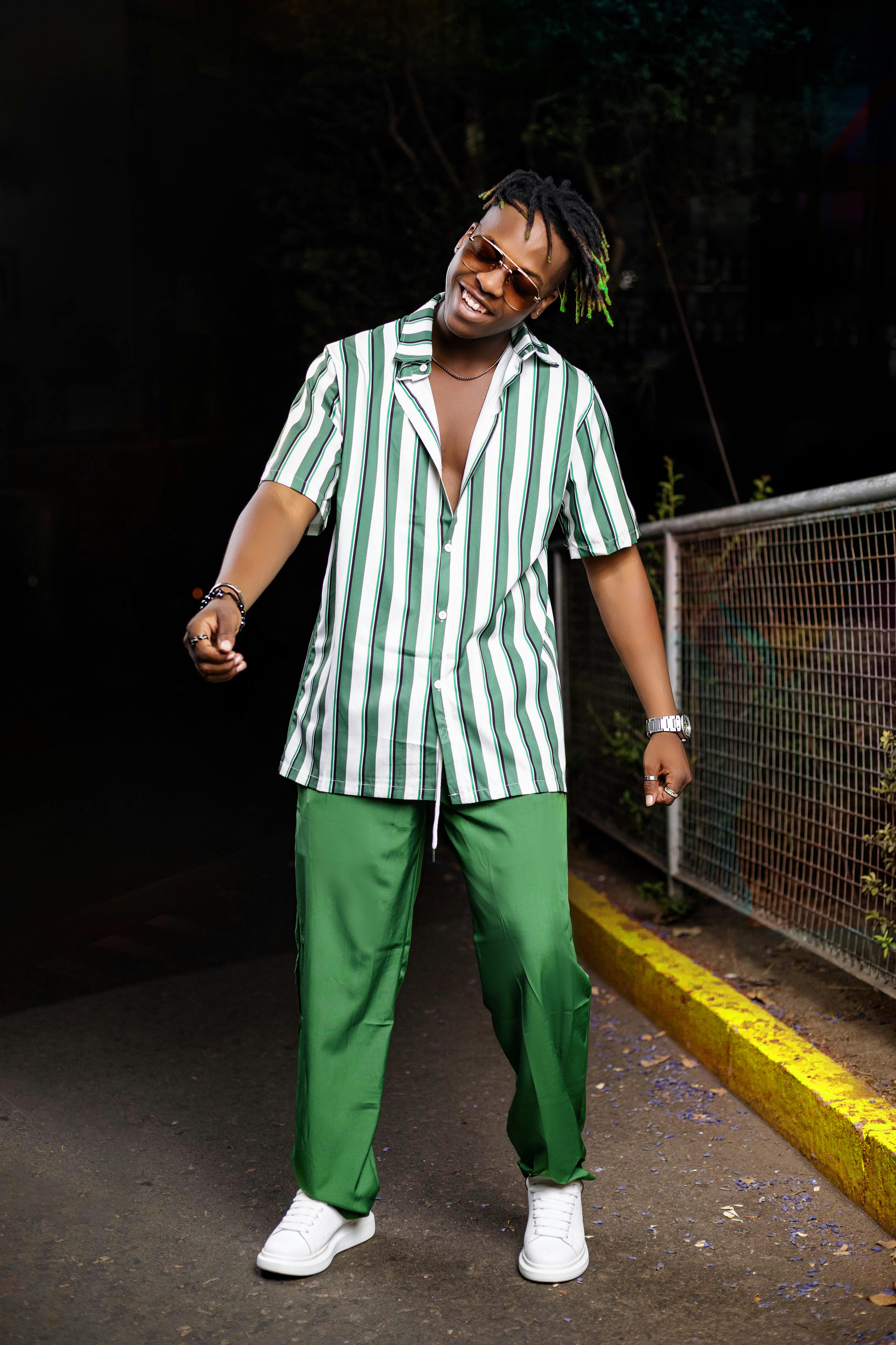 Stylish young man in striped shirt and green pants smiling and posing outdoors at night.