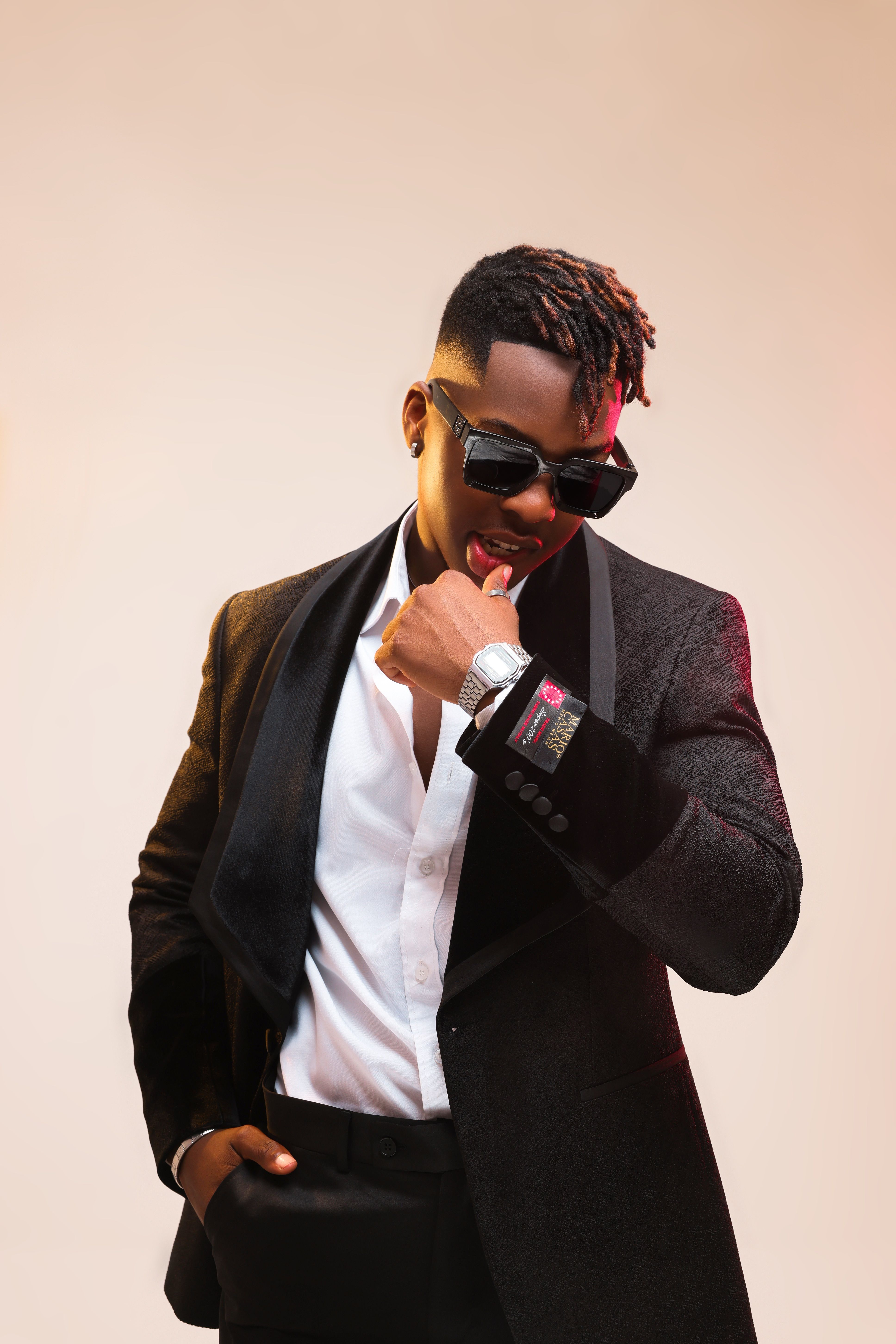 Confident man in formal black suit posing with sunglasses and a watch.
