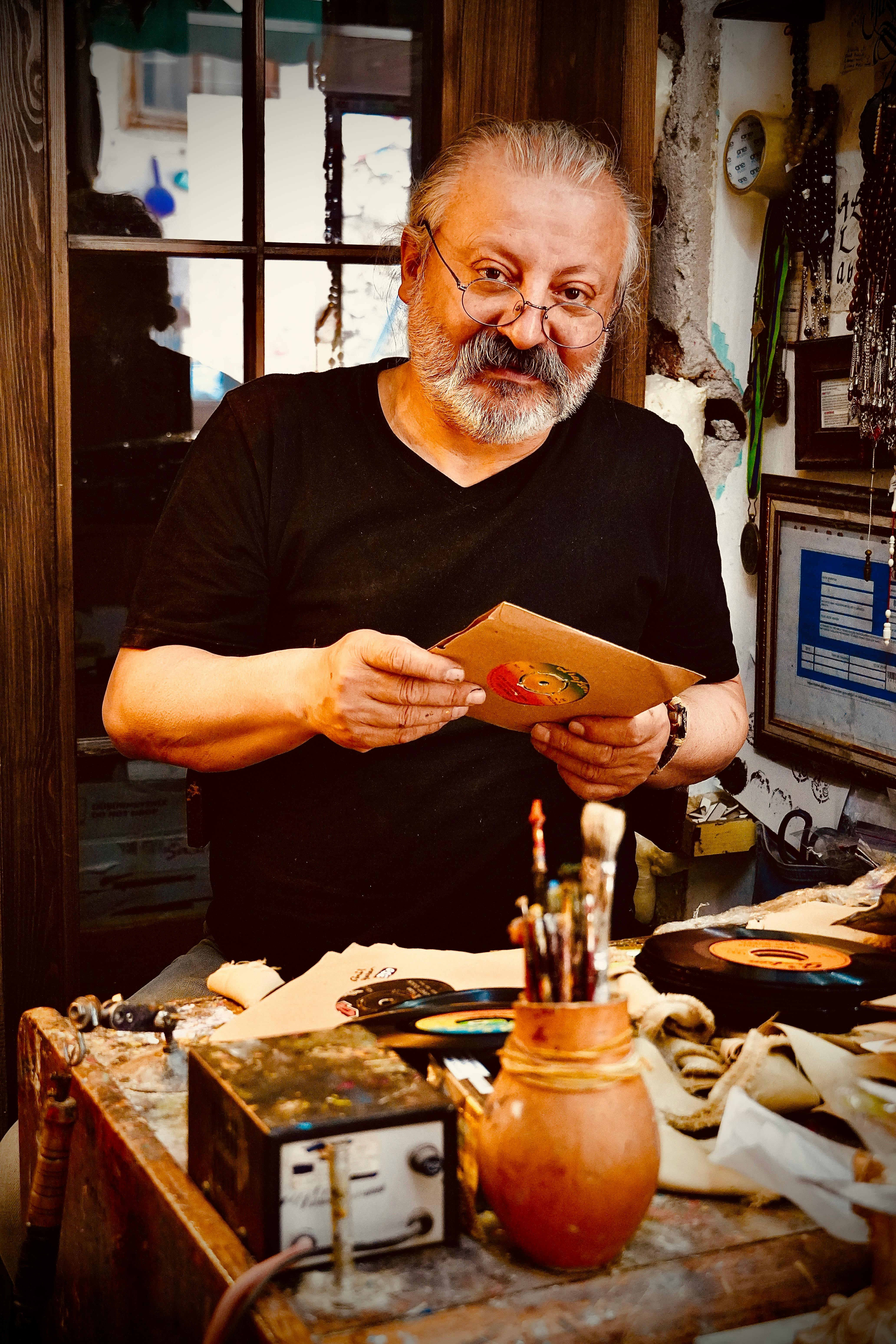 Bearded artisan in studio holding crafted piece amid creative workspace.