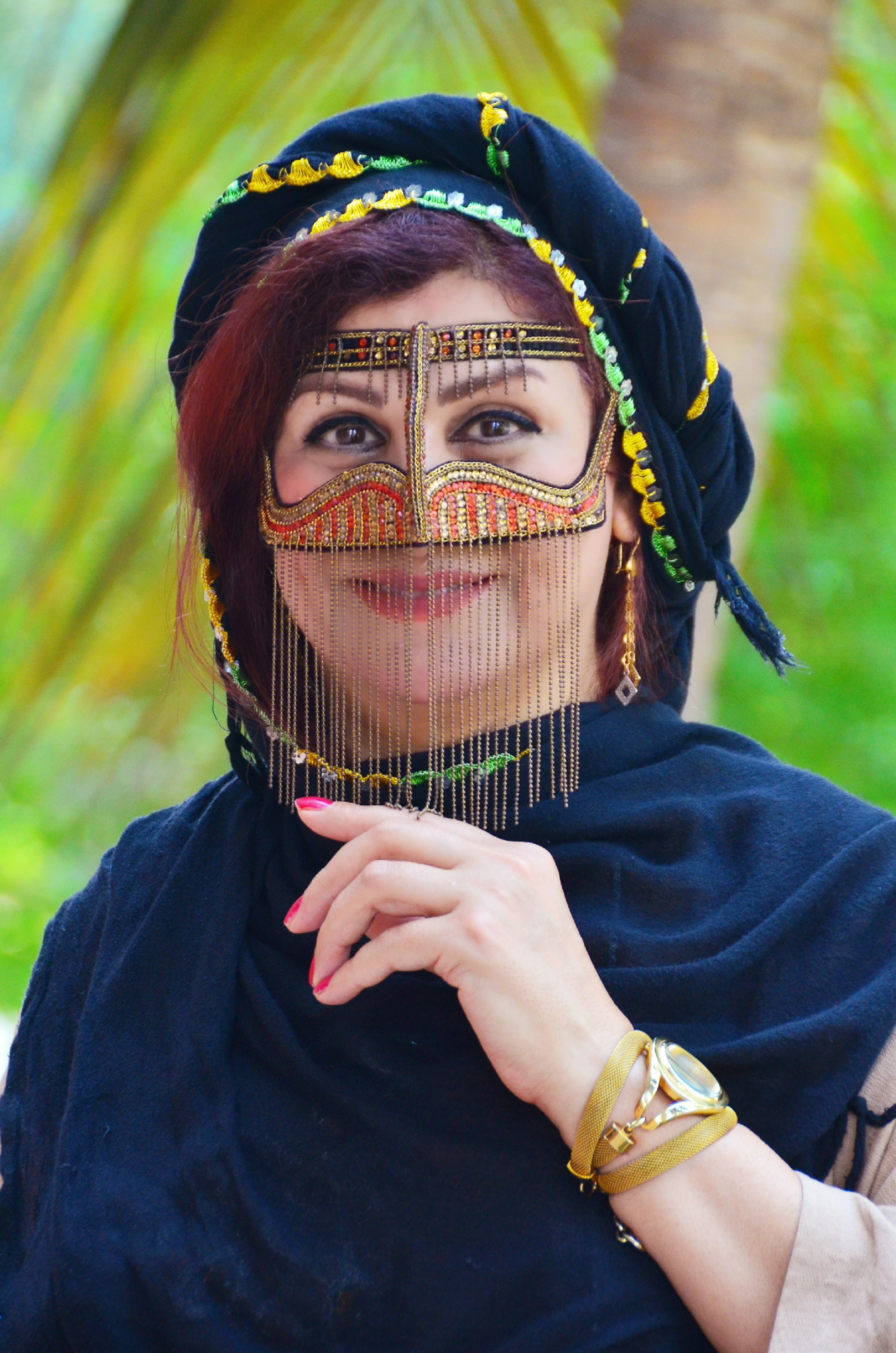 A woman wearing a traditional Middle Eastern burqa adorned with jewelry, standing outdoors.