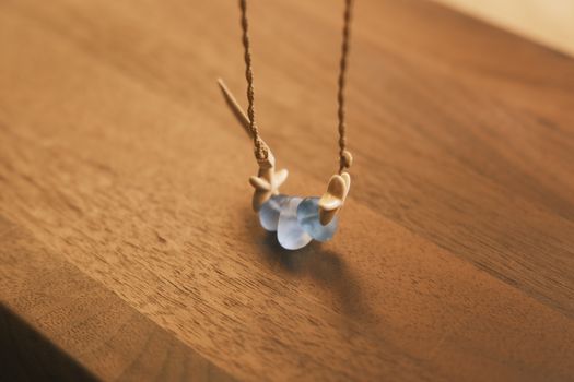 A beautiful handmade necklace featuring blue sea glass and shells on a wooden table, captured in soft light.