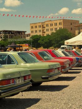 Row of colorful vintage cars at a sunny outdoor car show with spectators.