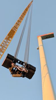 Tower crane hoisting a heavy wind turbine component at a construction site in Germany during daylight.