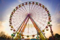 Vibrant Ferris wheel rising against a beautiful sunset sky in an outdoor amusement park setting.