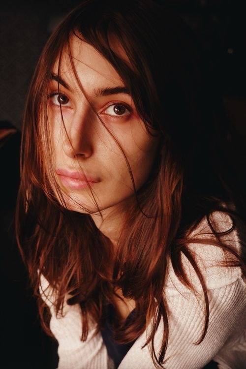 Free Moody portrait of a young woman with soft lighting and thoughtful expression. Stock Photo