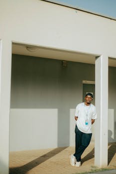 A relaxed portrait of a man standing in an open courtyard in Abuja, Nigeria, showcasing casual fashion.