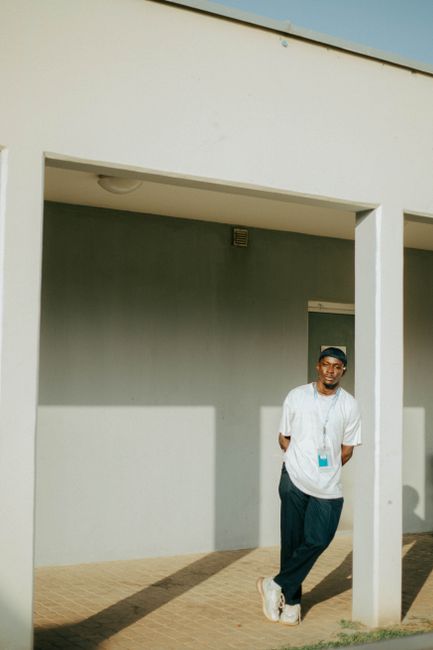 A relaxed portrait of a man standing in an open courtyard in Abuja, Nigeria, showcasing casual fashion.