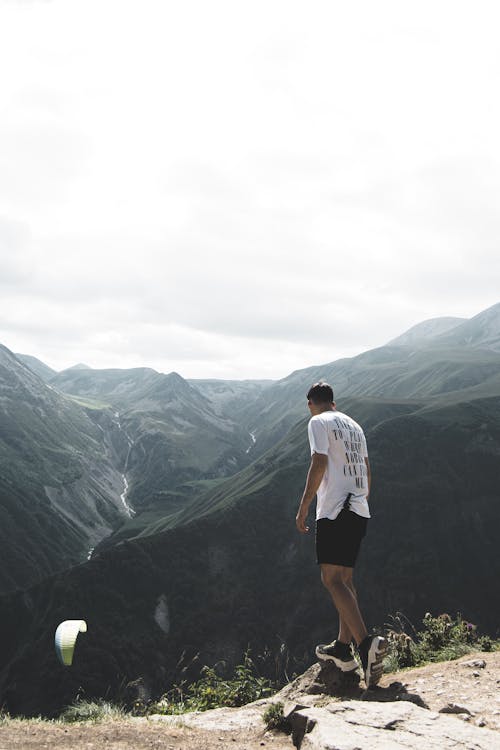 Man Wearing White T-shirt and Black Shorts Standing on Cliff