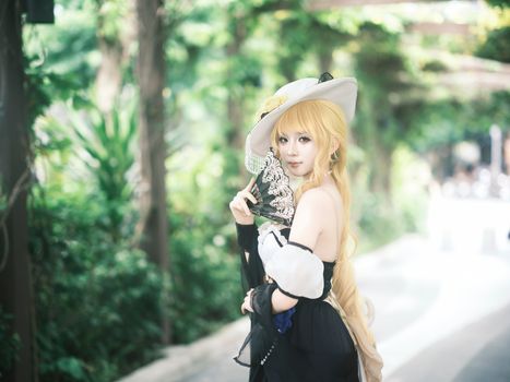 A captivating cosplay portrait of a woman in a stylish hat holding a decorative fan outdoors.