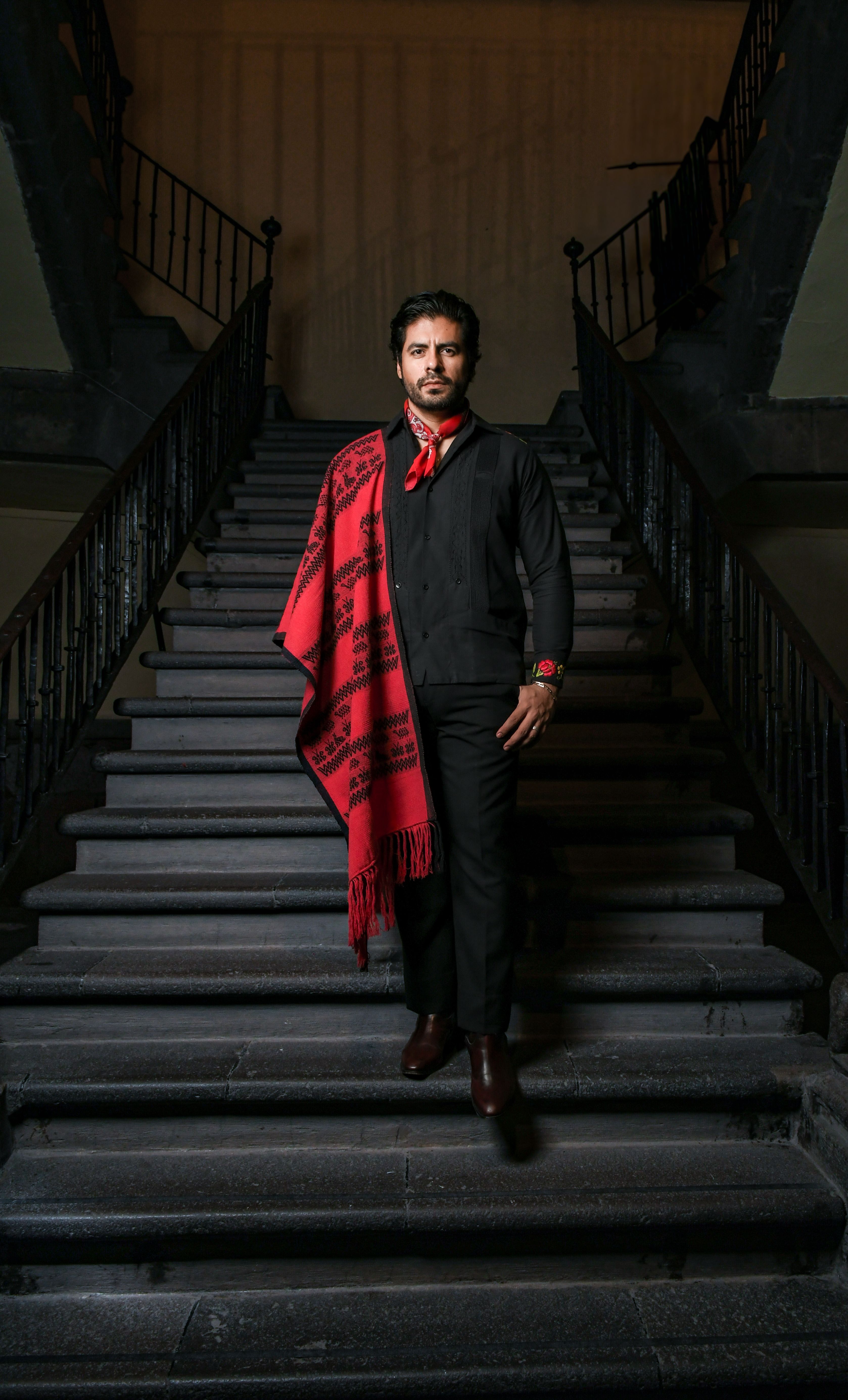 Portrait of a confident man in formal wear with red accents on a grand staircase.