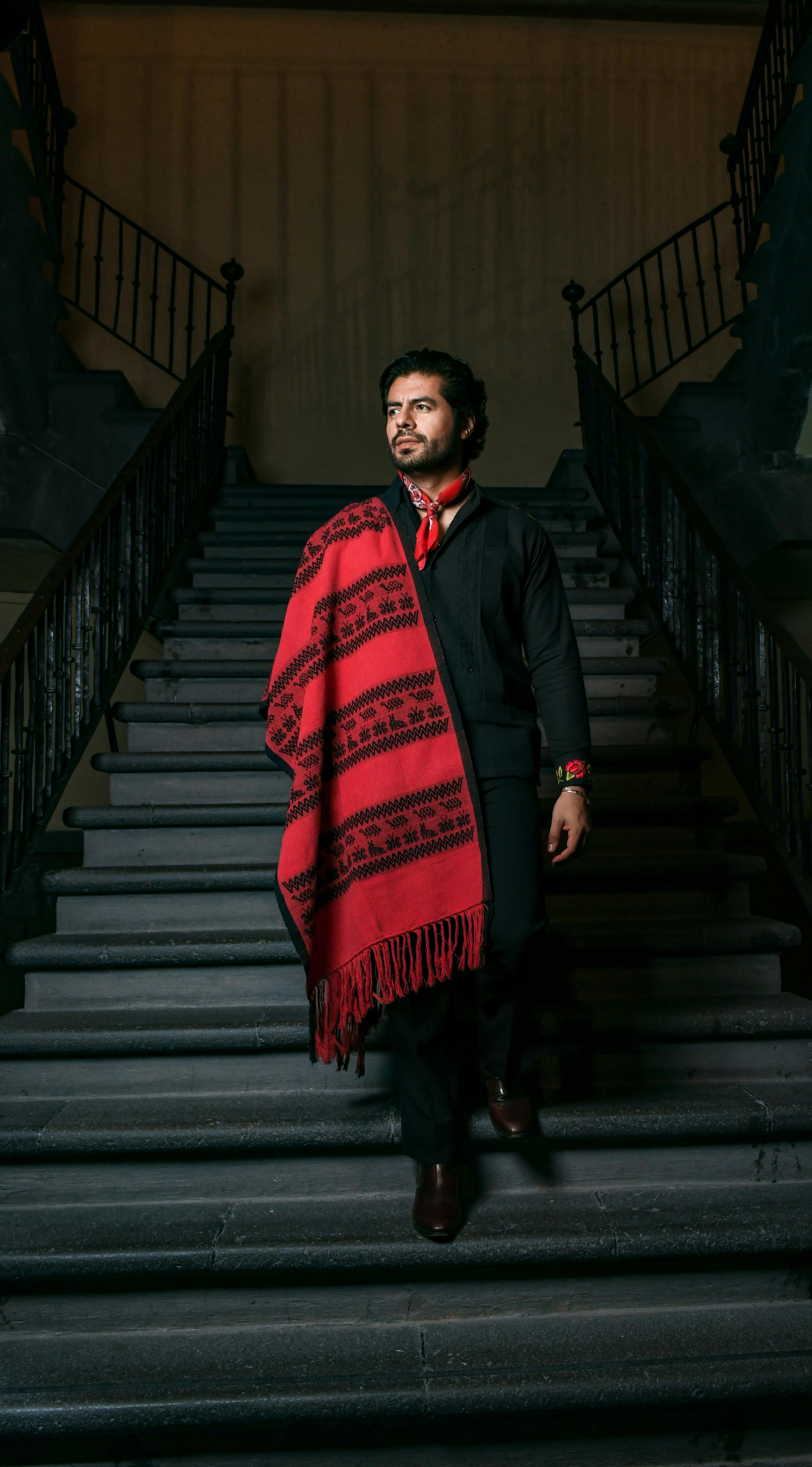 A man in ethnic attire with a red shawl descends stairway indoors, exuding style and tradition.