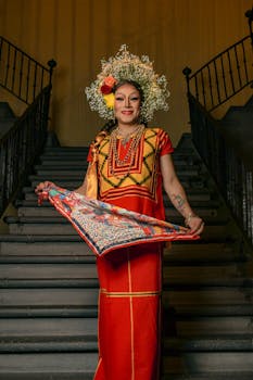 Portrait of a person in traditional attire with floral crown, standing on a staircase.