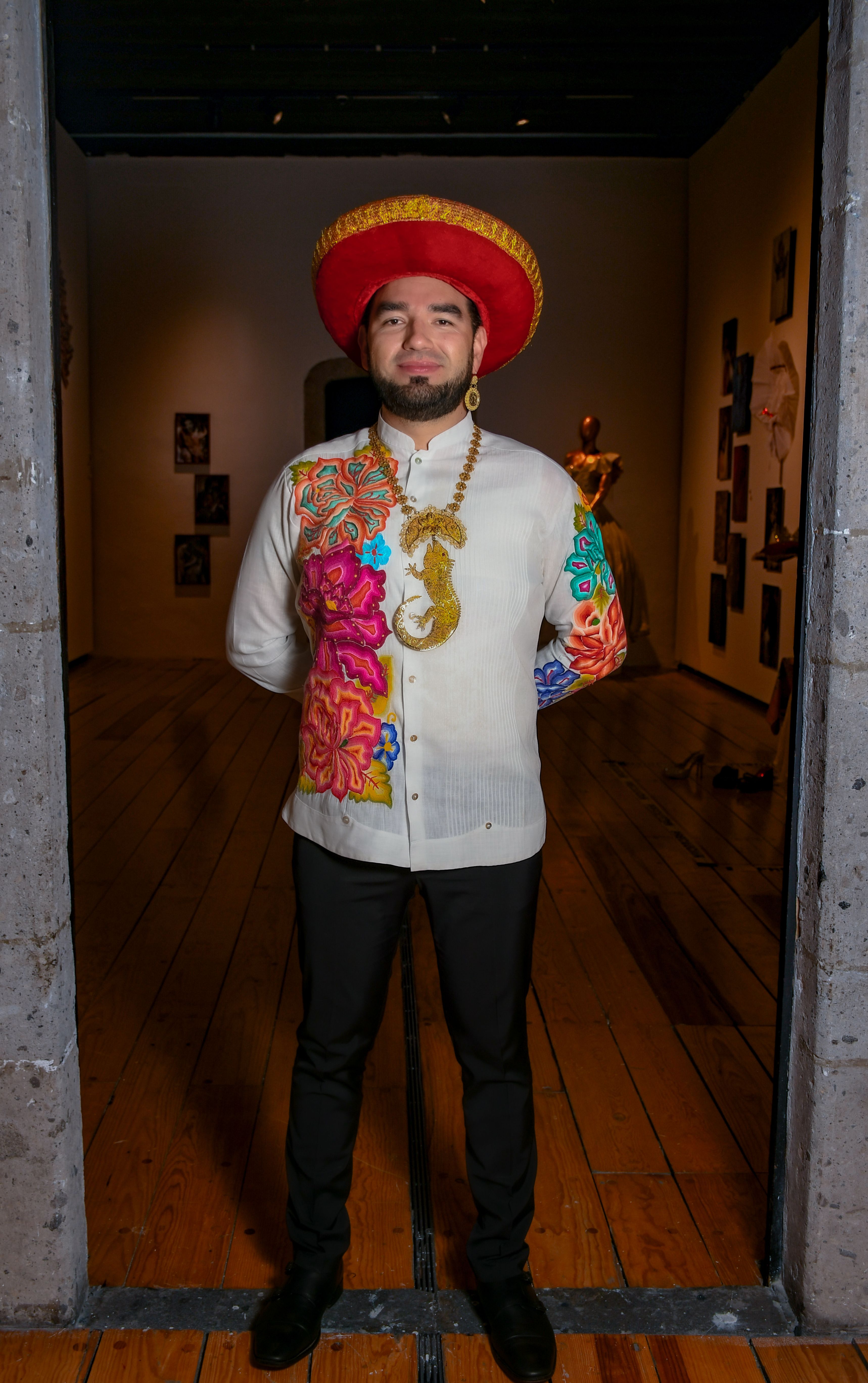 Man in colorful traditional attire standing in an art gallery. Cultural expression.
