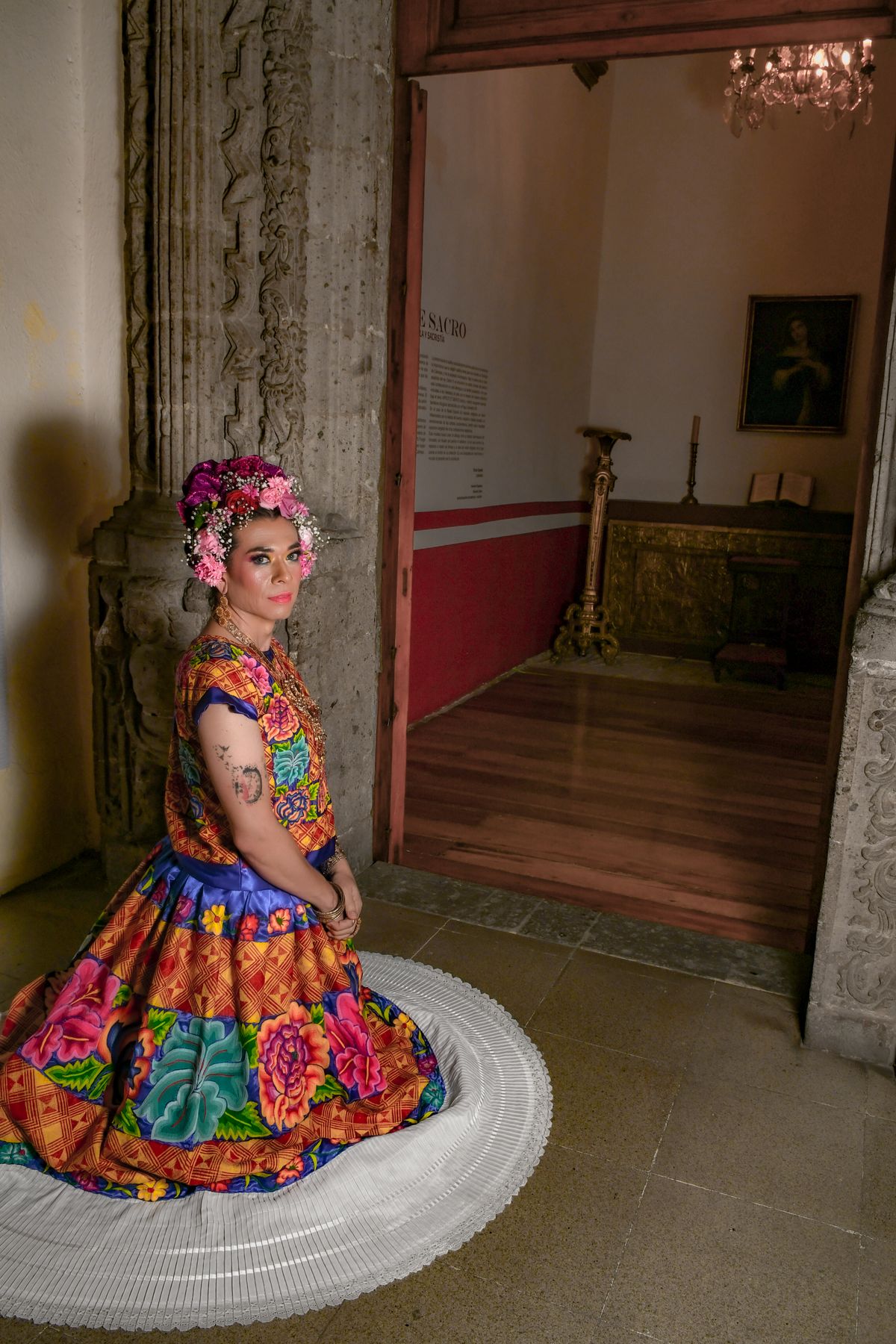 A woman in vibrant traditional Mexican attire poses gracefully at a historical site.