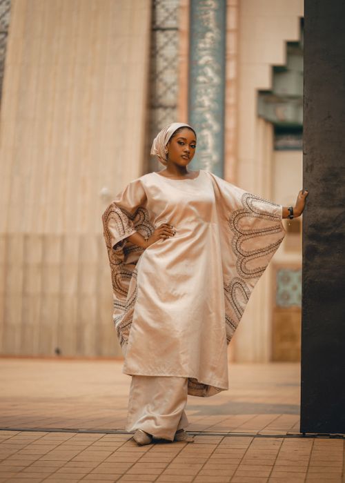 Free Confident woman in flowing beige dress posing against decorative architectural background. Stock Photo