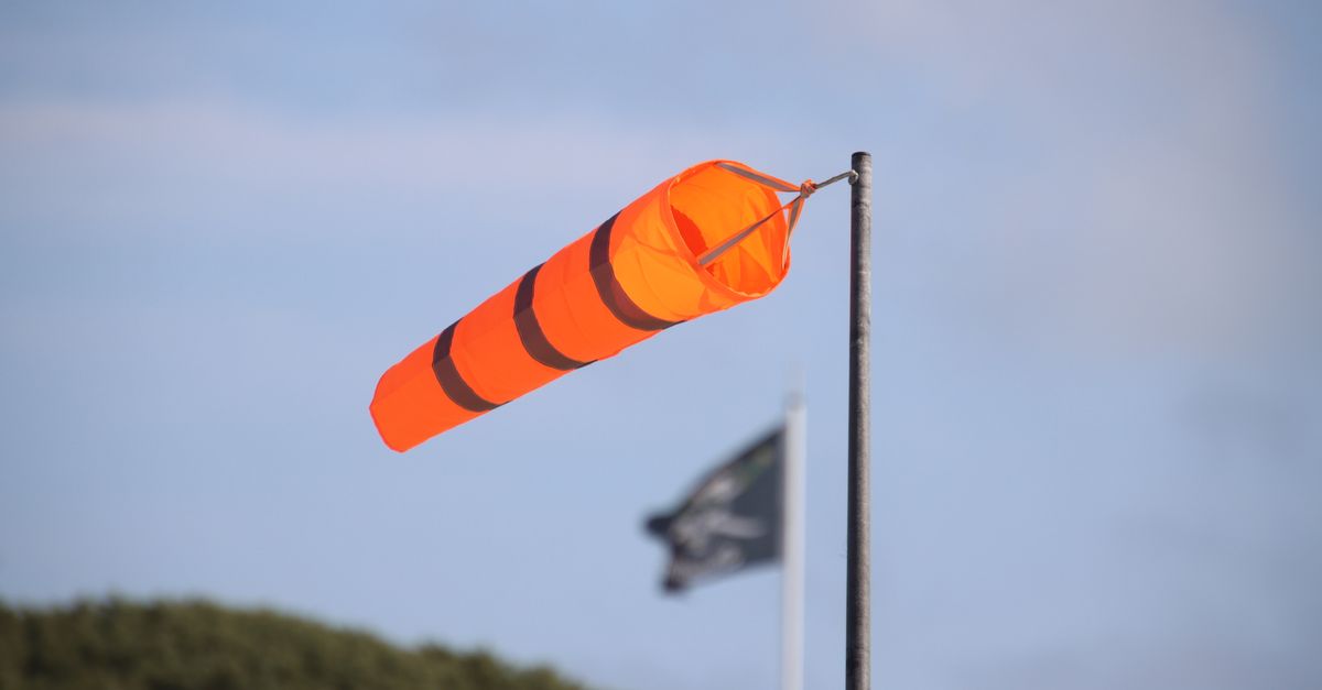 Bright orange windsock indicating wind direction against clear sky background.